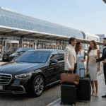 Friendly private chauffeur greeting a stylish couple with elegant leather bags next to a black Mercedes S-Class sedan at the Milan Malpensa Airport forecourt